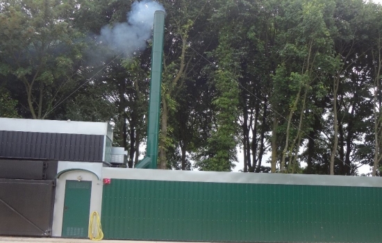 A green boiler house with a smoking chimney with trees behind A green boiler house with a smoking chimney with trees behind