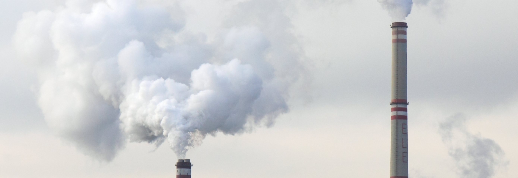 Chimney's with smoke coming out against a grey sky