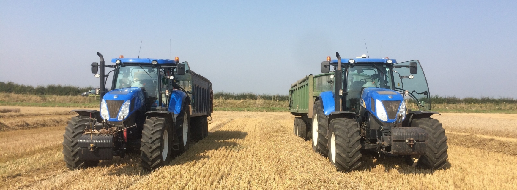 Two blue tractors in a field of straw