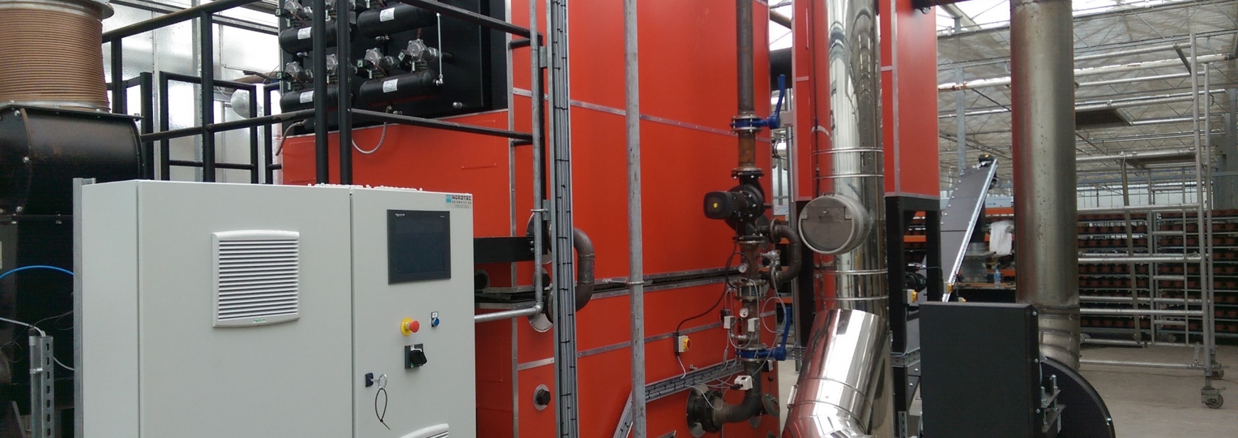 Large red biomass boiler with sliver pipes in a greenhouse