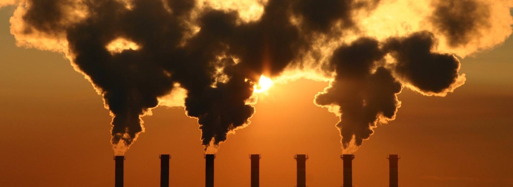 A factory with chimney smoking with a sunset behind